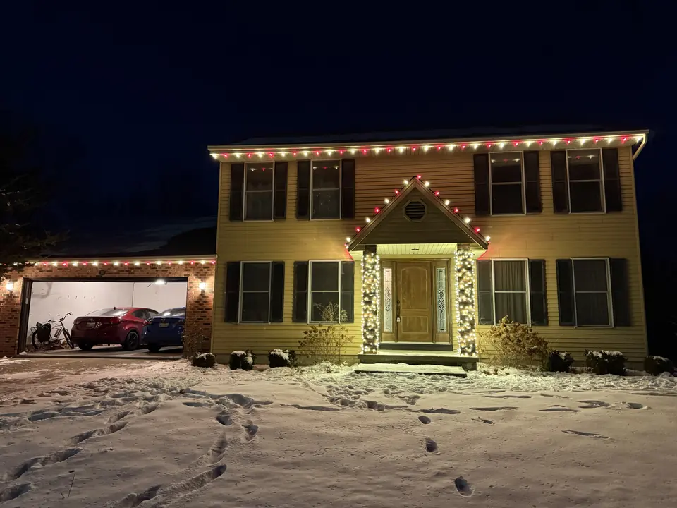 Two-story home with red and white Christmas lights on the roofline in the snow